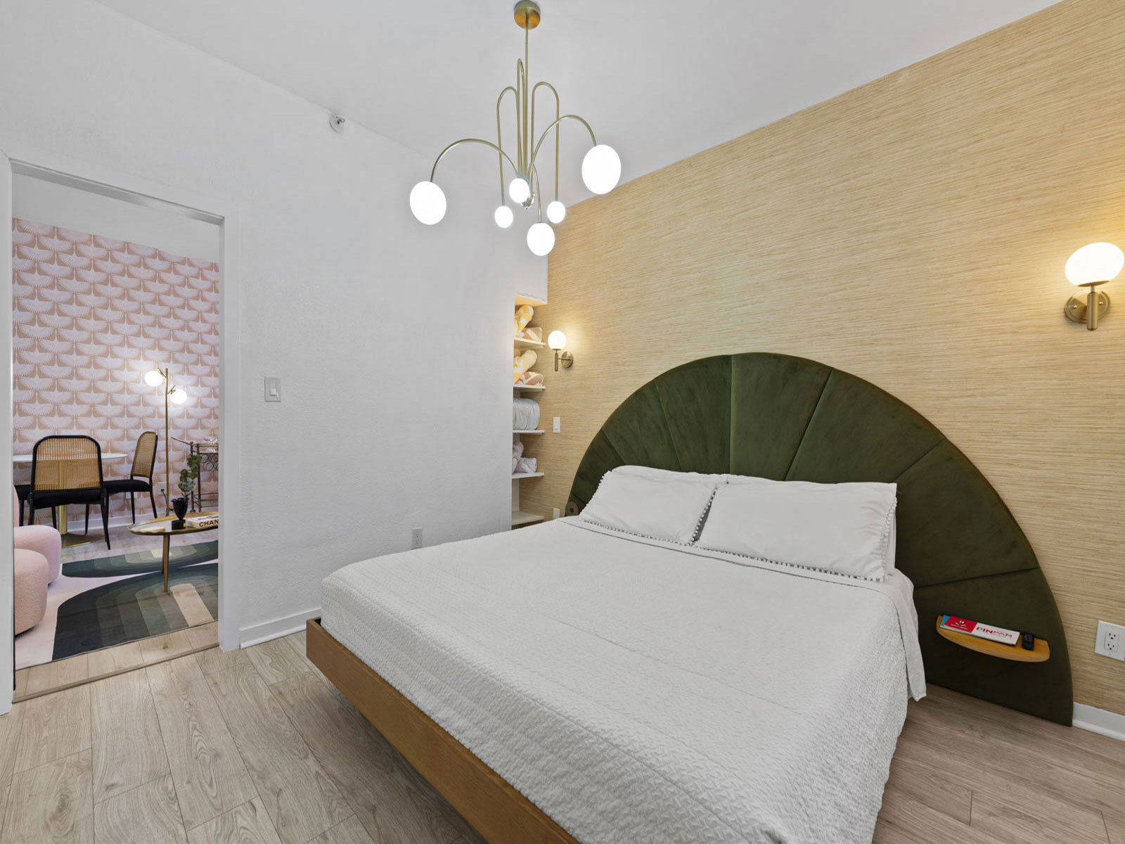 The bedroom of Unit 1E, with a green velvet arched headboard and grasscloth wall